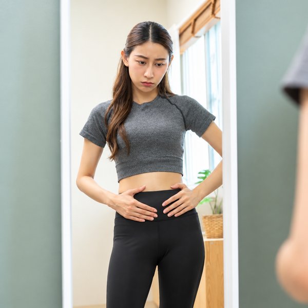 鏡の前でお腹を気にする女性